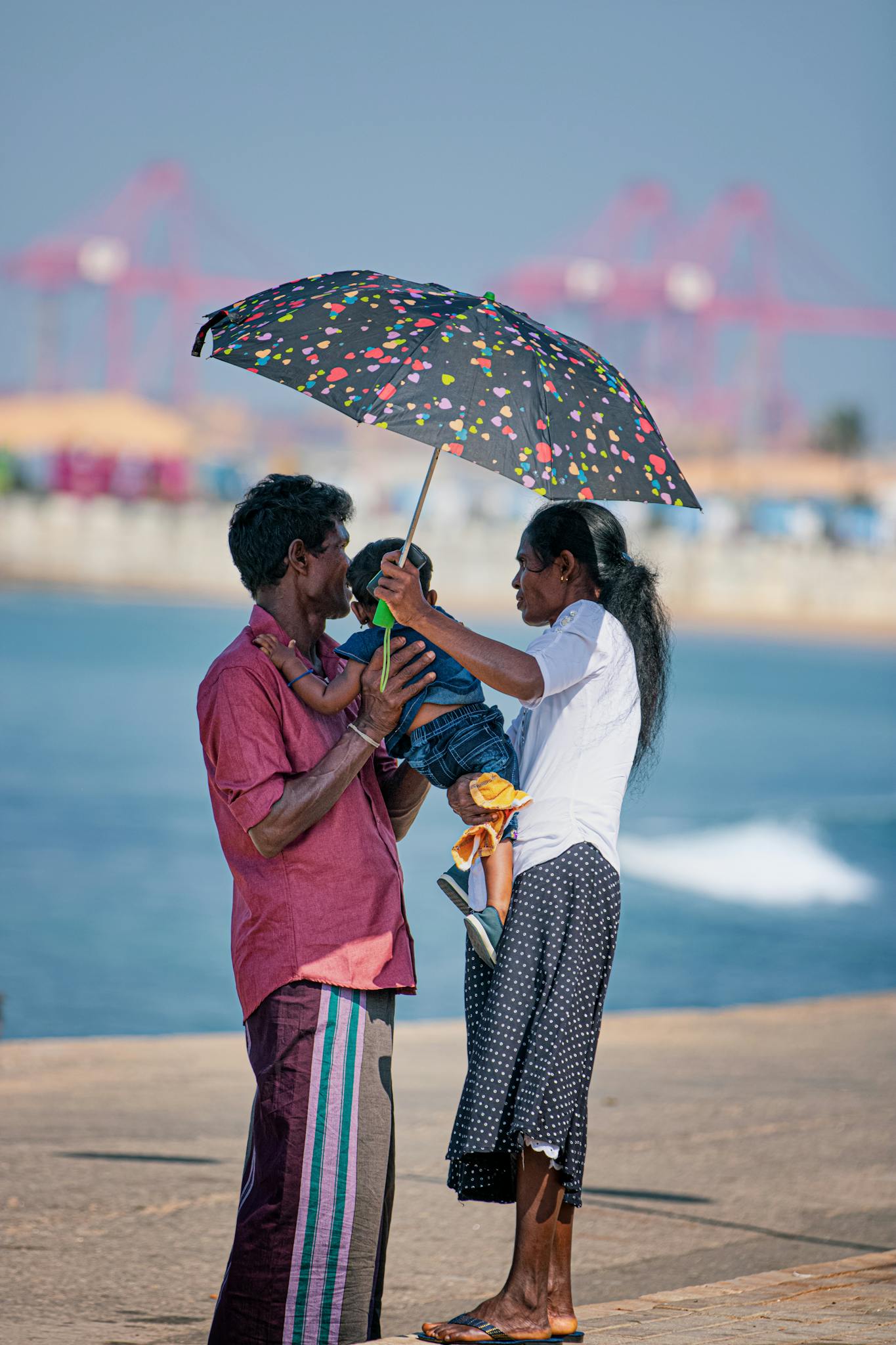 A family enjoys a sunny day by the sea with a colorful umbrella, capturing a heartwarming moment.