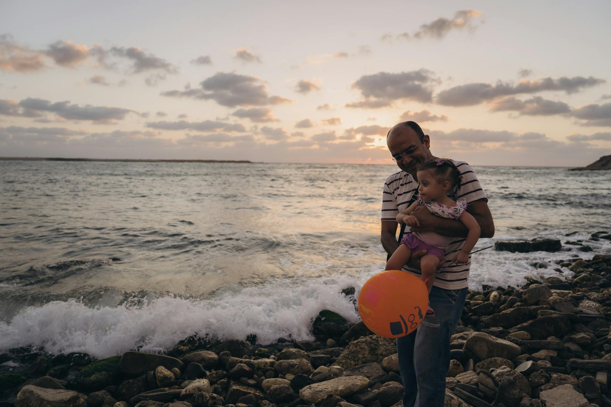 A heartwarming scene of a father and child enjoying the sunset on a rocky Alexandria seashore.