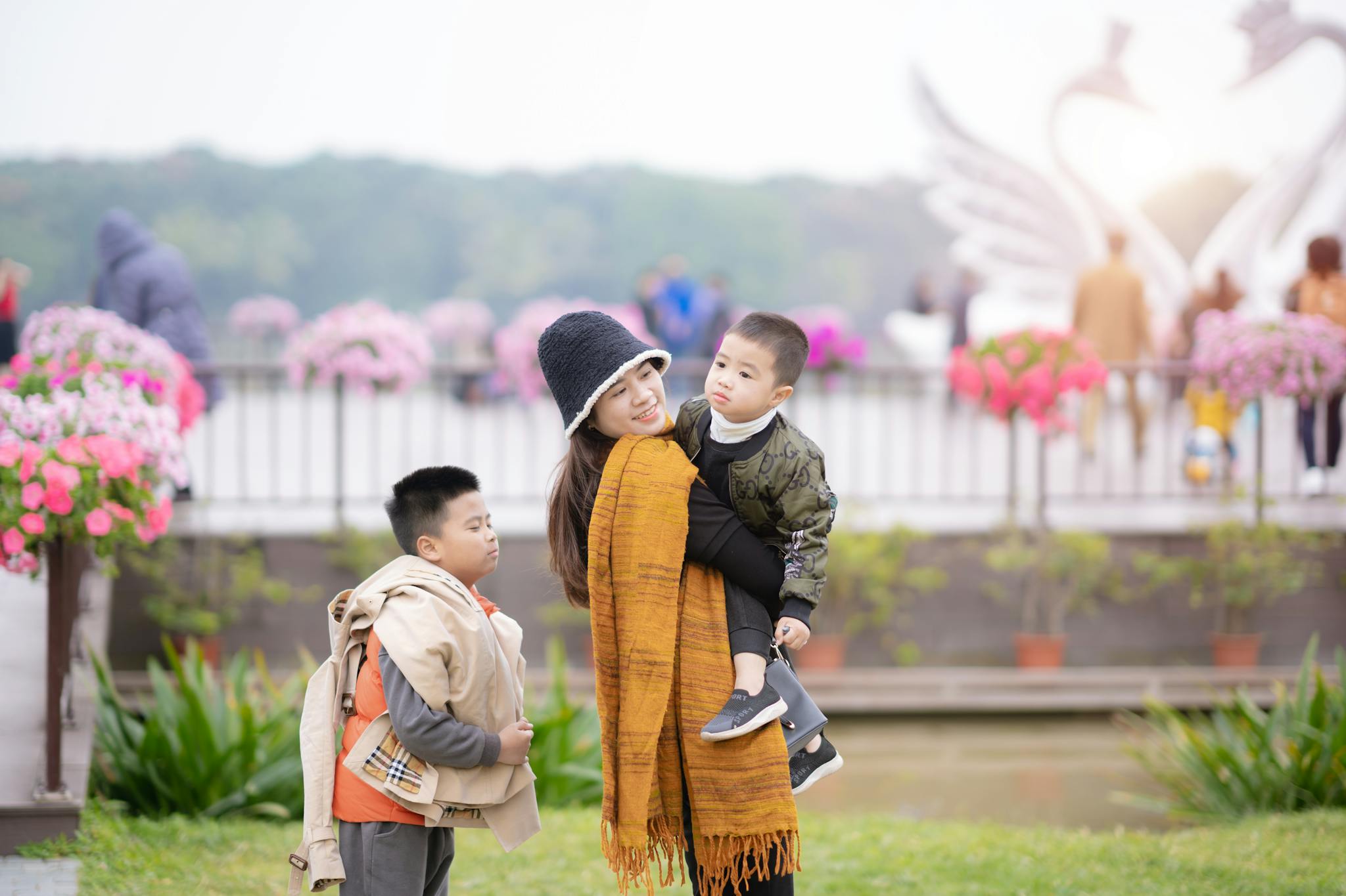 A smiling woman and two boys enjoying a walk amidst colorful flowers in a park.
